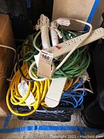 Tightly bundled extension cords and power strips in crate with a MaxSold tag labeled 'Ext. Cords.'
