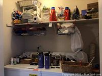 Wide view of the washer/dryer top surface, shelves with cleaning supplies, candles, Hydro Flask bottles, and an iron.