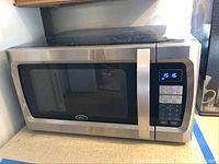 Closed view of Oster microwave showing stainless steel exterior with control panel and handle