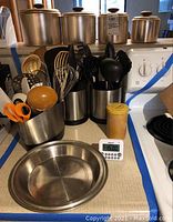 Overview photo showing the kitchen tools organized in four stainless steel containers along with a ceramic yellow-lidded container, vintage aluminum Mirro canisters, and the stainless steel pie plate on kitchen counter.