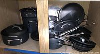 Photo of various pots, pans and lids arranged inside a cabinet showing the overall quantity and condition.