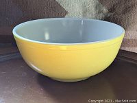 Side angled view of large yellow Pyrex mixing bowl showing bright yellow exterior and white interior.