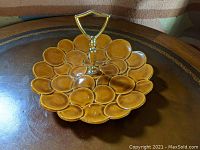 Front angled view of the circular tidbit server with bubble pattern and brass handle on wood table.