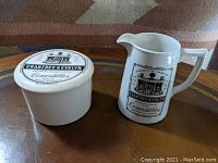 Porcelain creamer and covered sugar container displayed on table, showing front black printed Crabtree & Evelyn design.