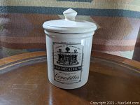 Front view of white porcelain cylindrical tea canister with vintage black printed Crabtree & Evelyn storefront design and text on front.