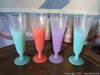 Front view of four pilsner glasses showing two teal, one orange/red, one lilac/purple glass with gradient color designs.