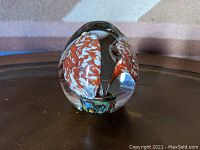 Front-angle photo of the art glass paperweight showing the two mottled orange and white flowers with multicolor base inside clear glass dome.