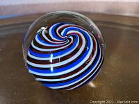 Top angled view of glass paperweight showing red, white, and blue swirl pattern inside spherical clear glass.