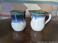 Front view of creamer and sugar set showing blue and white drip glaze, placed on brown surface with patterned background.