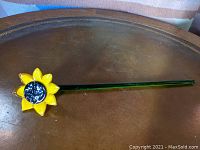 Full view of long stem yellow glass sunflower laid on a wooden surface.