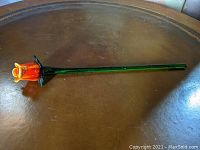 Long stemmed orange tulip glass flower on wooden surface, full length view.