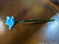 Full view of blue glass flower with long green stem on a table.