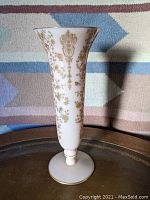 Front view of creamy white Cambridge Glass trumpet vase with intricate golden Rose Point design and gold rim on base, sitting on table.