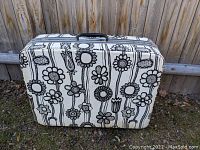 Front view of the large hard shell vintage Samsonite Fashionaire suitcase with black and white floral flower pattern on cream background.