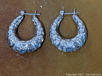 Pair of large hammered sterling silver modernist hoop earrings shown open with square post clasps visible.