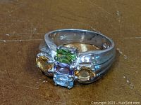 Front view of the sterling silver ring, showing five colorful stones in prong settings including green, light blue, purple, and yellow stones.