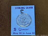 Sterling silver Gemini zodiac pendant on blue card displaying zodiac name and dates