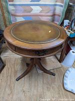 Full view of round mahogany drum table showing leather top with gold embossing and carved wood edge detail.