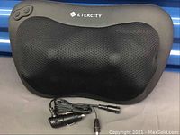 Black Etekcity shiatsu neck massager shown front facing with mesh cover and two buttons, accompanied by car adapter cable.