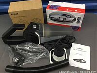 Overview of Kutime car vacuum cleaner with flexible hose, filter, accessories, and original box of the car MP3 player and Aukey dash camera box in background.
