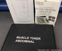 Three items boxed in the health lot: muscle toner abdominal box in black, blood pressure monitor box, and leg air massager box.