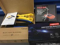 Boxed electronic tools and accessories including balance lader, compression tool, anti spy detector, and blue light blocking glasses.