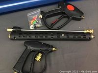 Photo showing complete set of two black pressure washer spray guns, a long perforated wand, and a bag with colored nozzle tips laid on a gray surface
