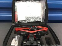 Sports magnifier glasses with bright red frame, adjustable black lens assembly marked 2.5X-R, placed inside foam-padded carrying case along with accessories like nose pads and small tools in plastic bags.