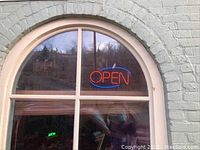 Neon "OPEN" sign mounted inside a window, showing red letters and blue border illuminated.