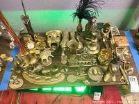 Overview of a wide variety of brass decor items on a table including animal figurines, candlesticks, masks, vases, and small decor pieces.