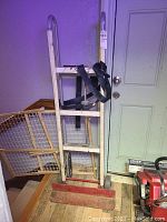 Full view of the appliance dolly standing against the wall by the door, highlighting overall structure and attached black straps.