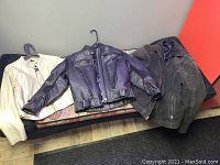 Three women's motorcycle jackets laid flat: white/light cream jacket, black leather jacket, brown suede jacket with visible white marks
