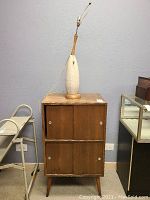 Full view of textured ceramic lamp on wood base atop record cabinet with two sets of doors