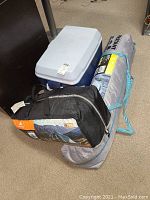 Photo showing the cooler and the two tents in bags on the floor.