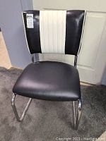 Front view of the mid-century chrome dining chair showing black solid vinyl seat and black and white vinyl backrest with vertical stripes.