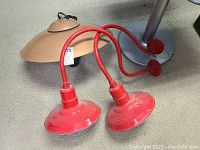 Photo of two red gooseneck light fixtures with curved arms, glossy red exterior, and one rust-colored metal shade seen behind.