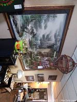 Large framed Asian landscape painting hung on the wall above various home decor items, showing its size and mounting.