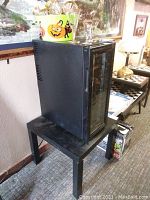 Side view of the black Haier wine fridge on a black table showing a Halloween bucket and glasses on top.