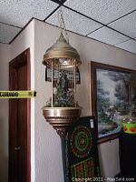 Front view of entire waterfall lamp hanging from ceiling, showing brass-tone canopy, chains, waterfall strings, decorative house and greenery