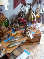 Photo showing brass table lamp with dome shade, two metal fish sculptures and bird painting on rock slab on wooden table.