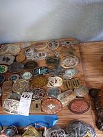 Top view of many belt buckles arranged on a wooden surface, showing variety in shape, size, and design