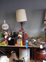 Overview of table with two gumball machines, carved wood totems, medallions, vintage lamps, and other collectibles.