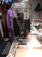 Front view of octagonal glass necklace display case showing six necklaces on a black velvet bust inside.