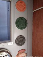 Three Aztec calendar plaques mounted on a gray wall: terra cotta, green, and gray colors visible. Half of a colorful Aztec mask shown below calendars.