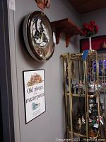 View of Seiko clock, wooden wall shelf above, and framed sign on grey wall with adjacent curio cabinet.