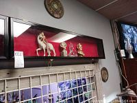 Photo of one black wooden framed rectangular hanging display case with glass front and red interior backing containing various decorative figures
