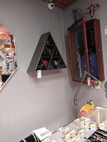 Wall display of metal triangular shelving unit containing nine glass paperweights.