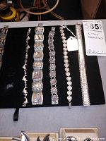 Five 925 sterling silver bracelets laid out on black mat showing different styles from dolphin links to gem accents.
