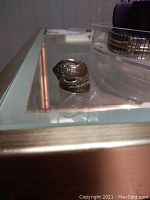 Sterling silver ring with a detailed floral and wave pattern placed on a glass table corner