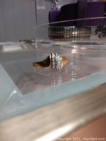 Gold-tone accented sterling silver ring with small stones displayed on glass surface.